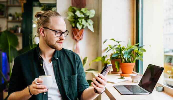 Mężczyzna pijący kawę i korzystający z telefonu komórkowego chronionego przez program Norton 360 for Mobile.